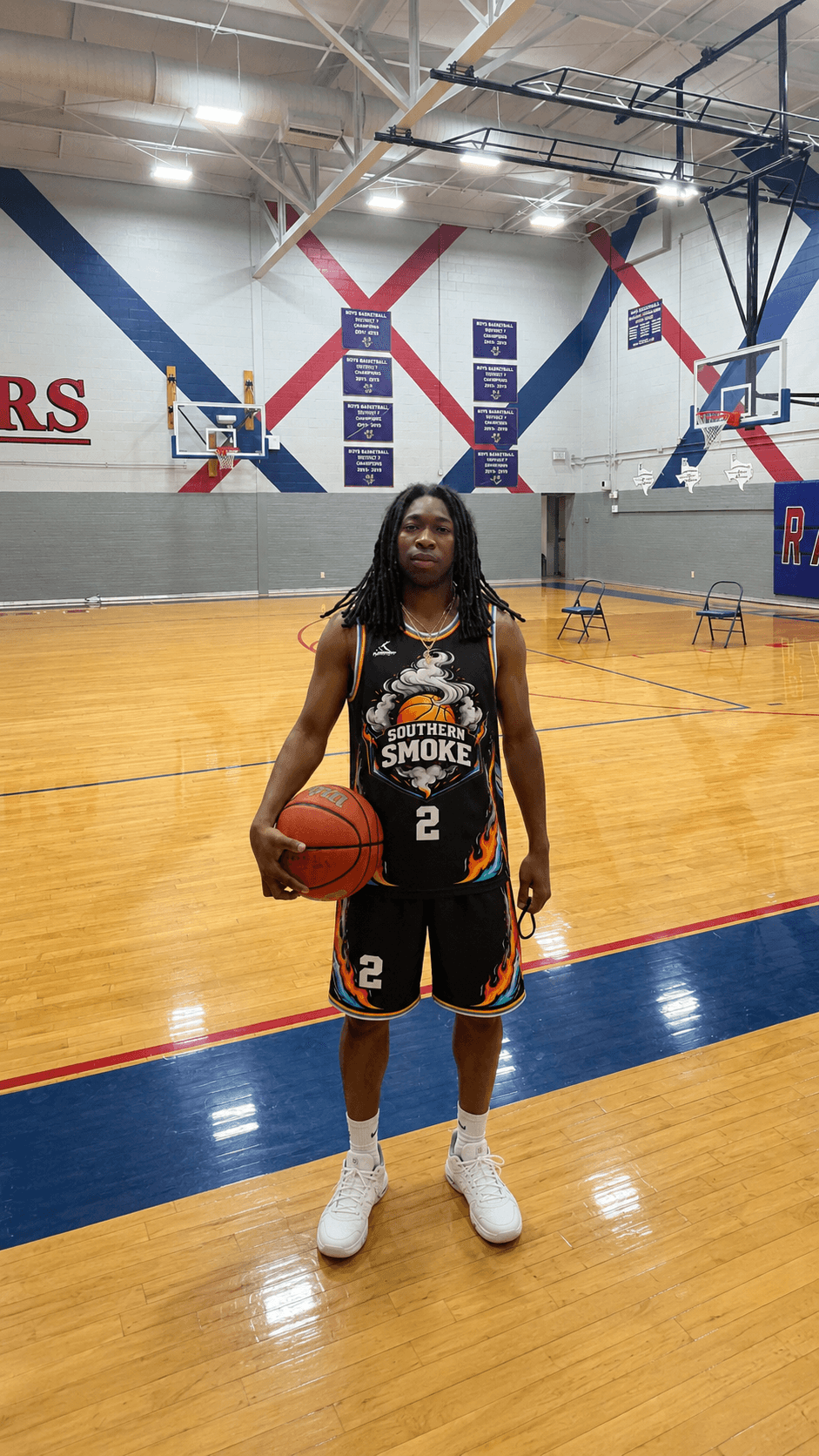Man in a black Southern Smoke uniform stands on a basketball court holding a ball.